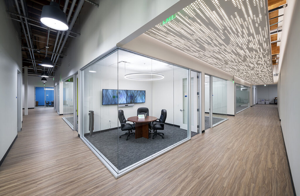 Interior office space with glass-walled conference room, wood paneled flooring and unique lighting
